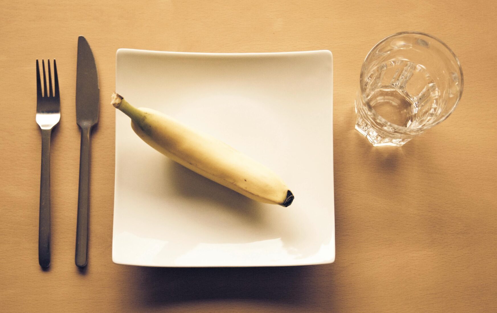 Jeden banan na talerzu i szklanka wody przedstawiają restrykcyjną dietę