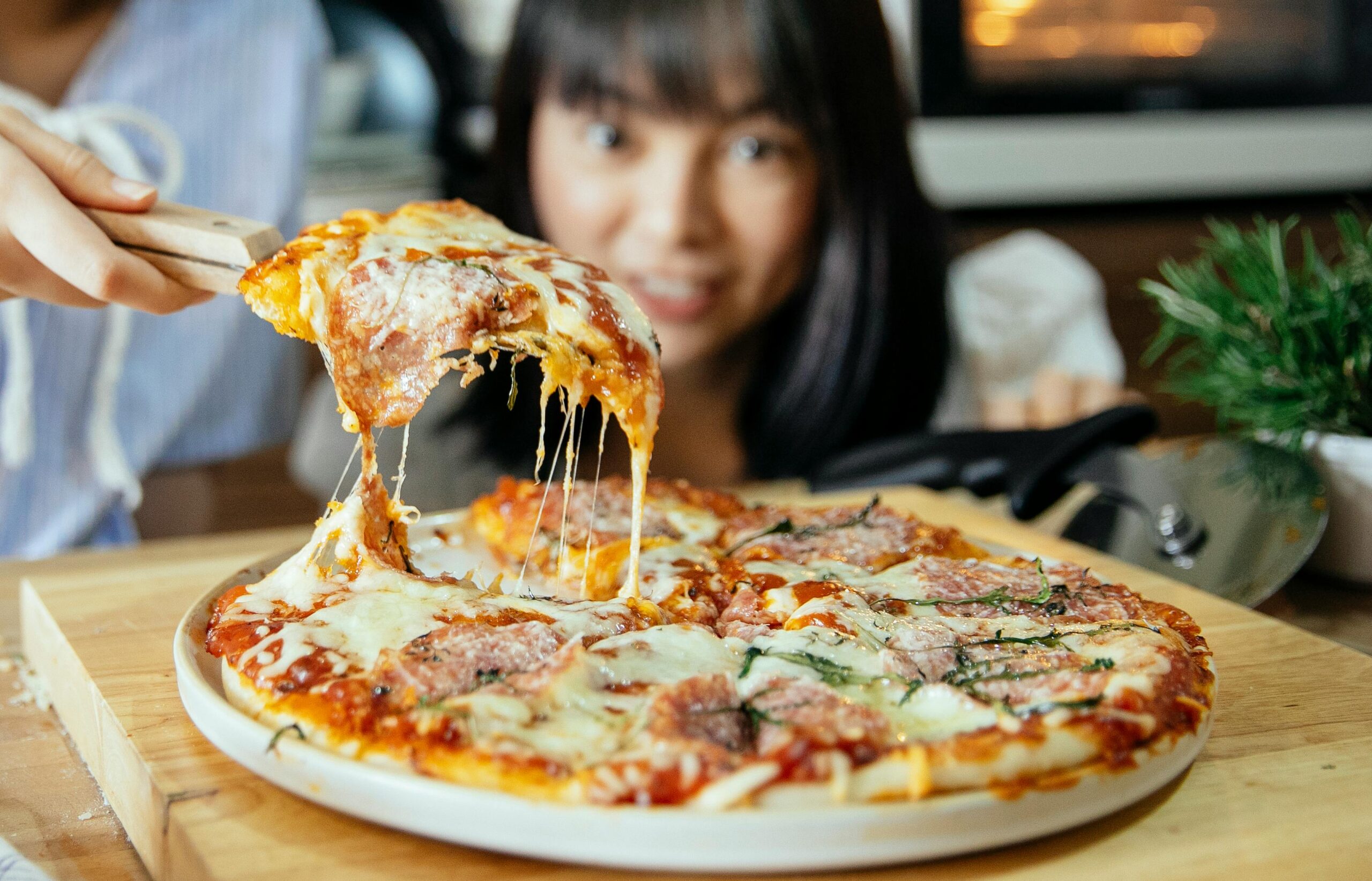 Przenoszenie kawałka pizzy, w tle dziewczynka wpatrująca się w pizzę