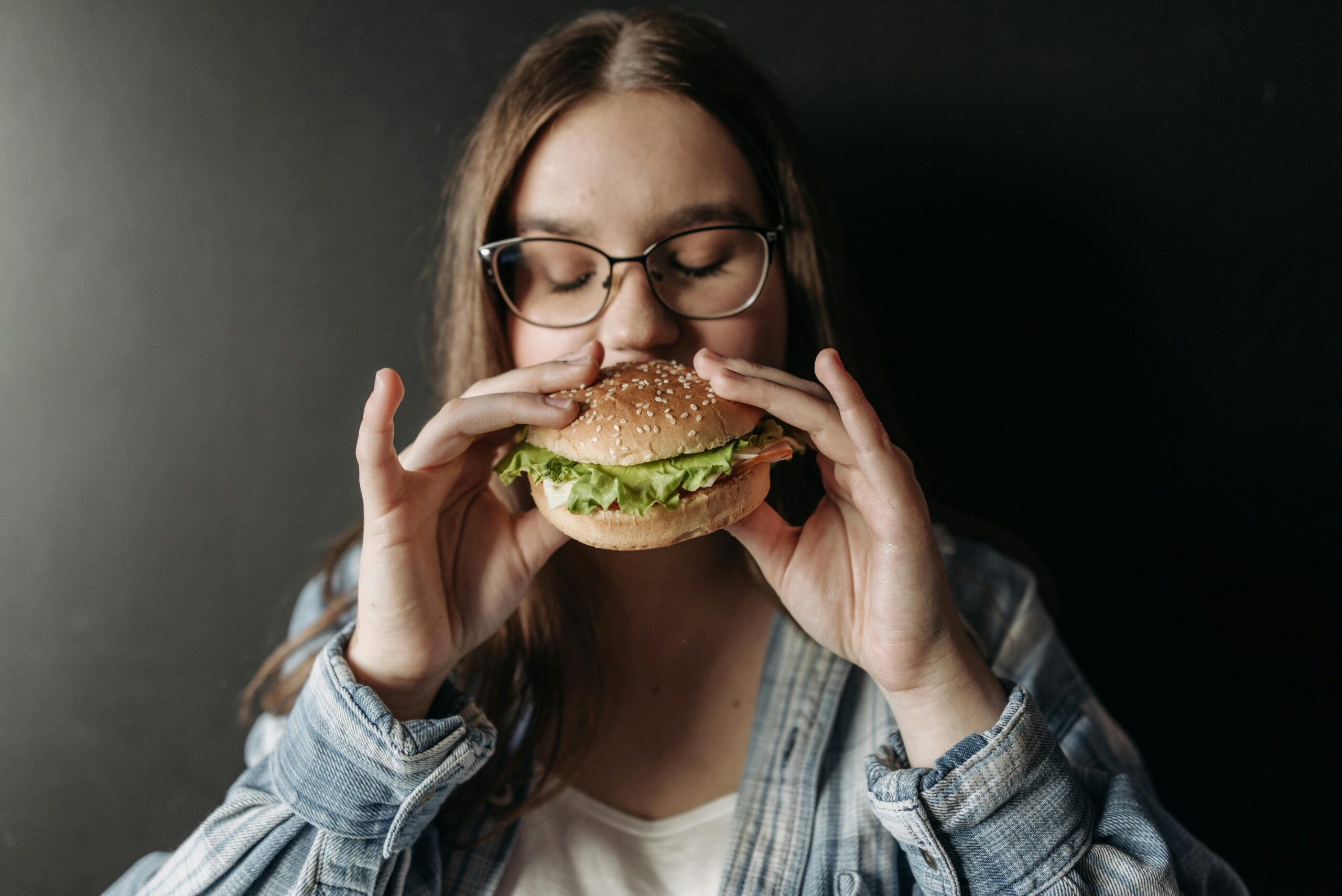 Czarne tło i dziewczyna, która je hamburgera. Napad objadania